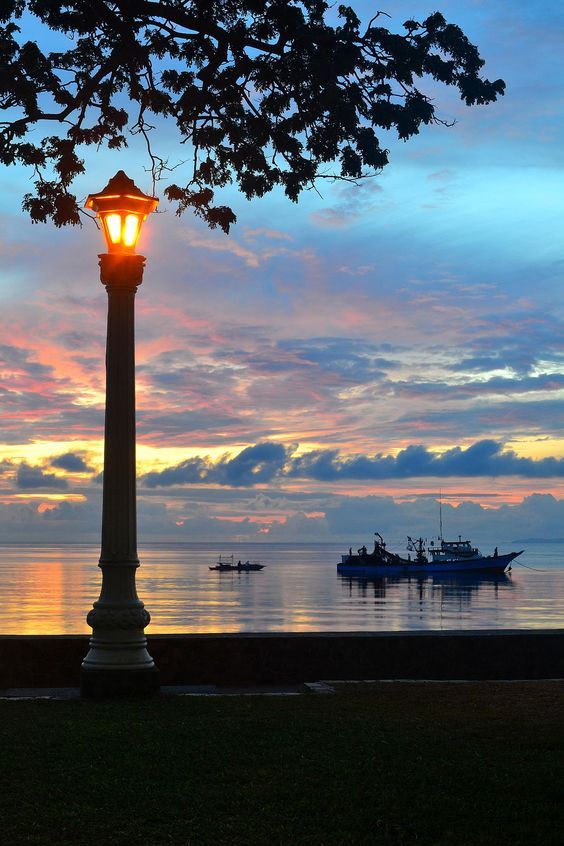 Rizal Boulevard in Dumaguete City at night with street food stalls, people walking by the seawall, and glowing streetlights by the sea.